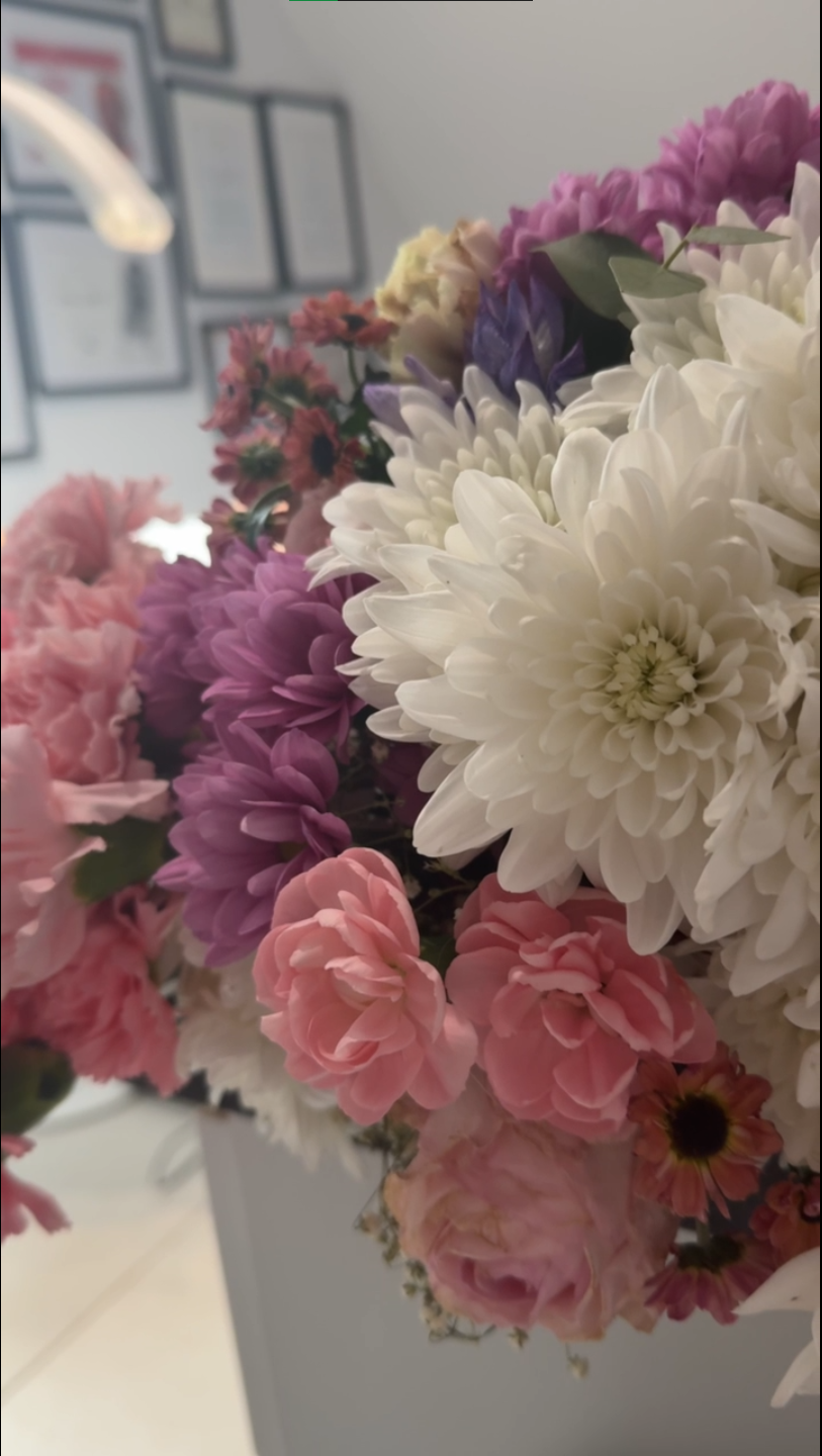 Zbliżenie na kolorowy bukiet z białymi, różowymi i fioletowymi kwiatami stojący w eleganckim wnętrzu.